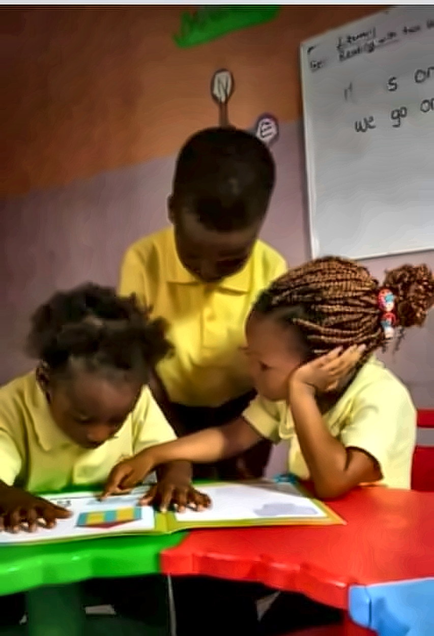 Three pupils leaning over a picture book together at a classroom table